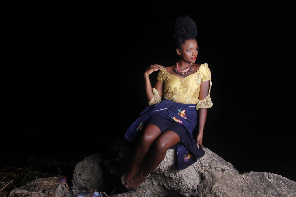 Ify Otuya sits on a rock, dressed in African attire George and jewelry.